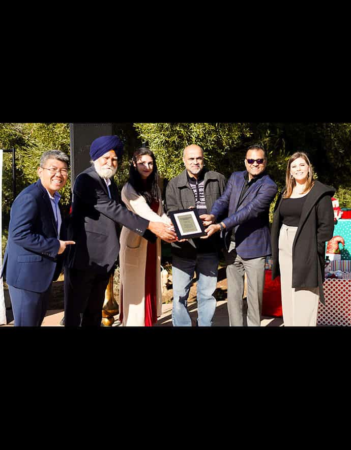 a diverse group of professionals present a framed award outdoors, with expressions of pride and teamwork.