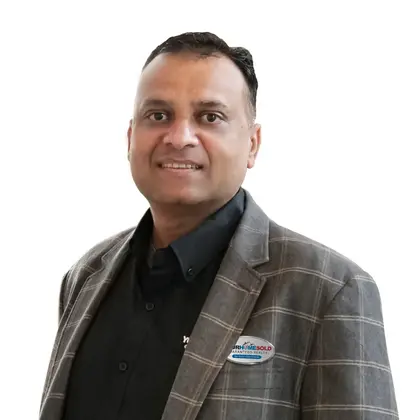 Sharad Gupta; Sharad Gupta, dressed in a professional plaid blazer and black shirt, with a 'Your Home Sold Guaranteed Realty' badge, smiles confidently.